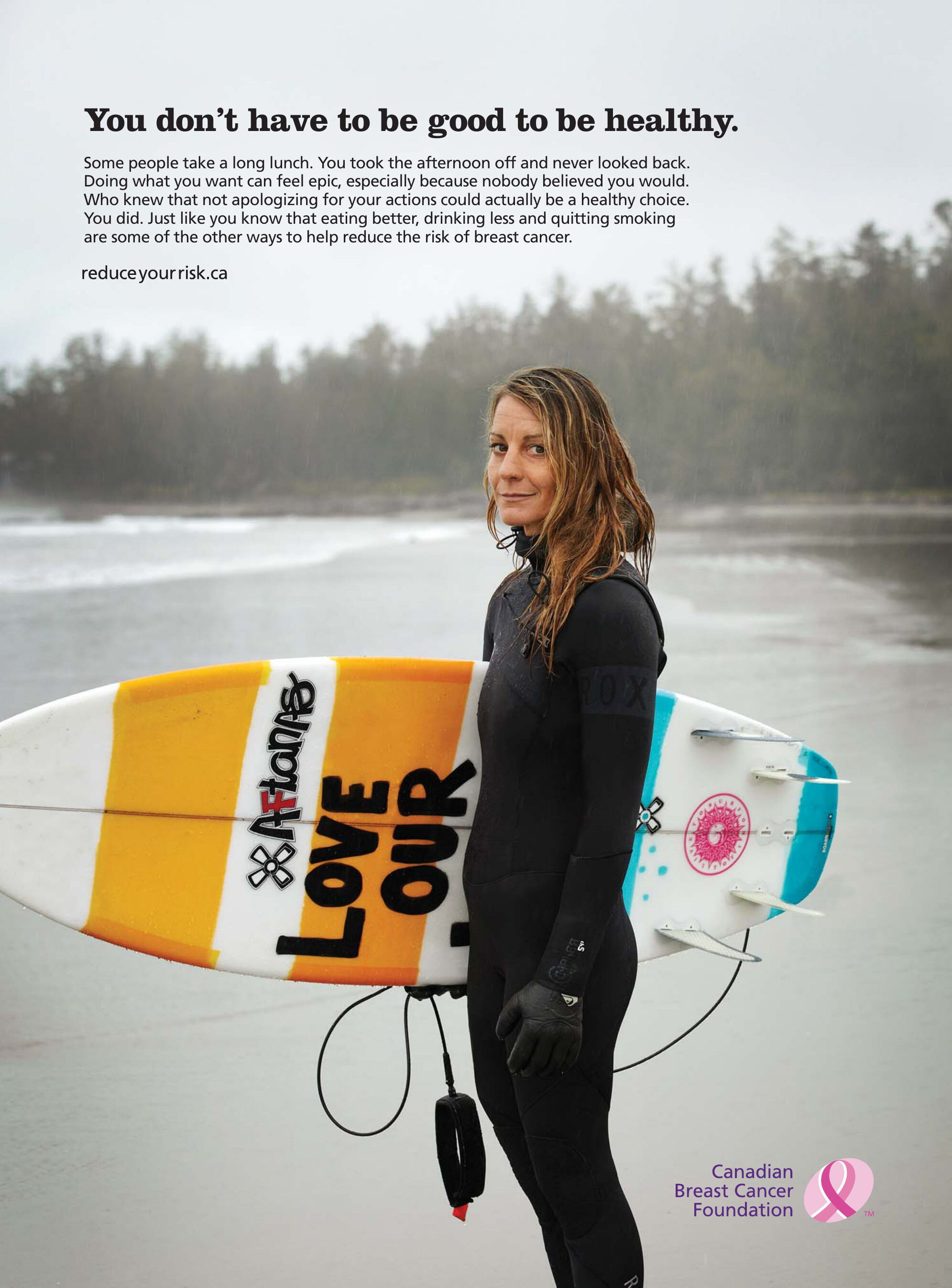Print ad: a woman in a wetsuit carrying her surfboard on a rainy Pacific beach, headline reading you don't have to be good to be healthy