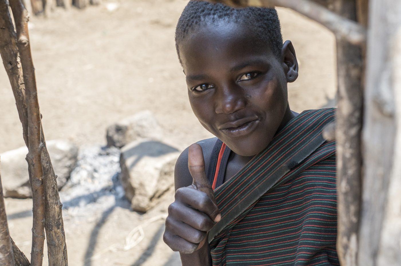 A young Karamojong boy giving a thumbs up and a slight smile to the camera