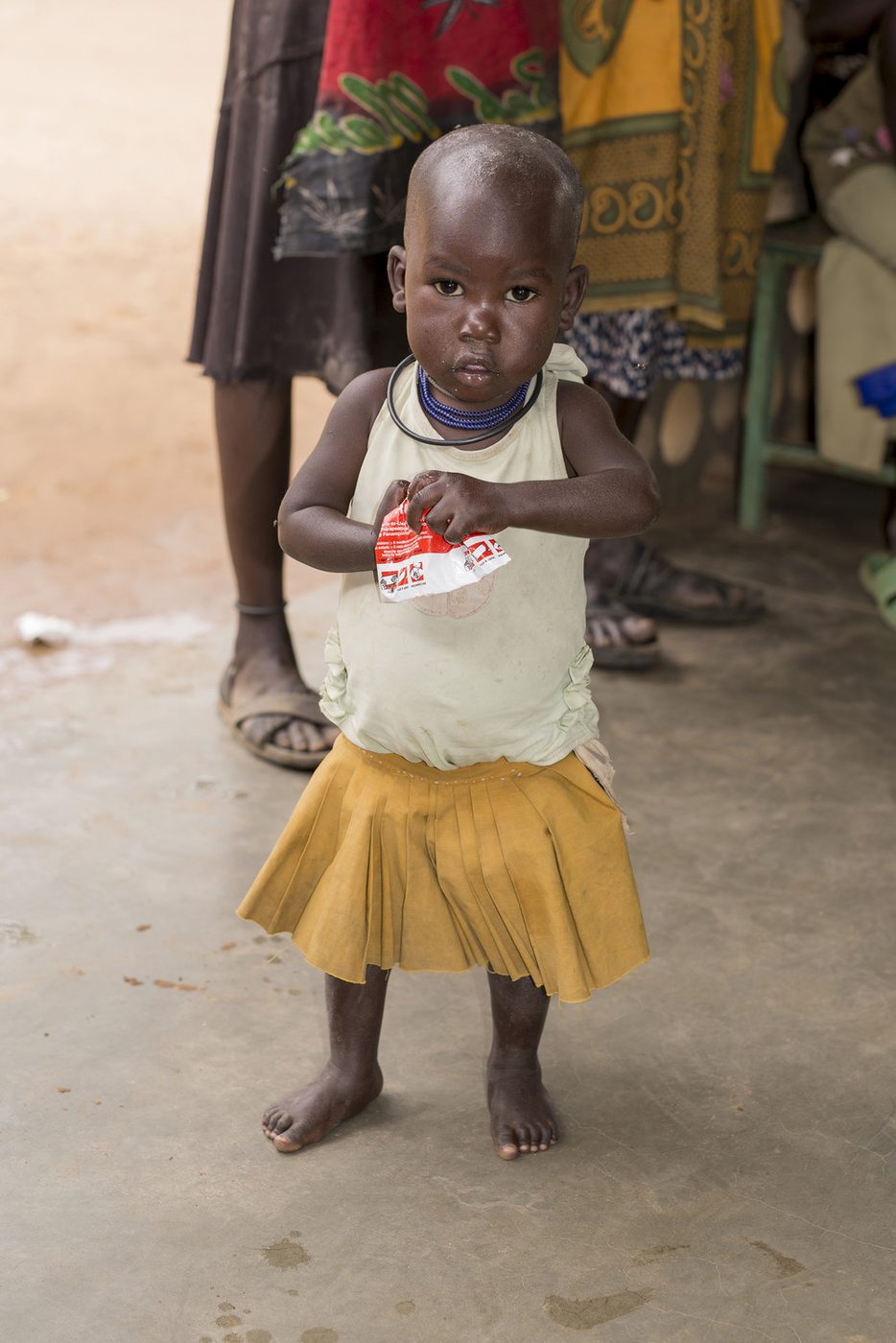 Aliat, now recovered, standing in a yellow skirt and holding a Plumpy Nut supplement wrapper