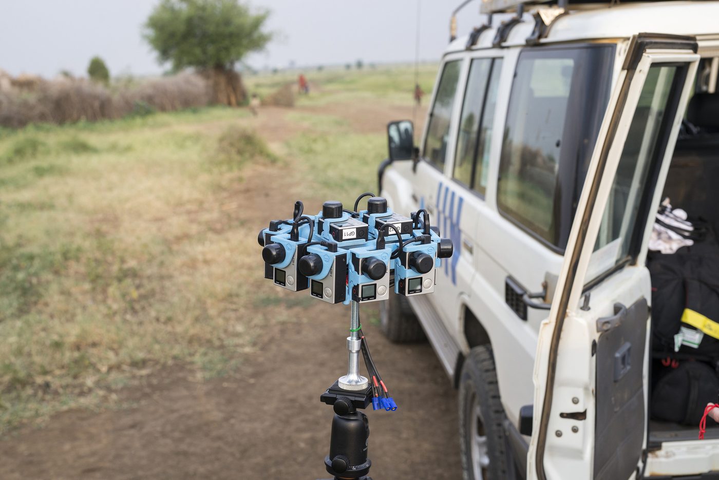 The 360-degree camera rig set up on a tripod beside a white UN Land Rover on location